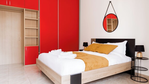 Een moderne slaapkamer met een houten bed, een rode garderobe en een ronde spiegel aan de muur.