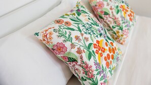Een bed met witte lakens en twee kleurrijke bloemenkussens.