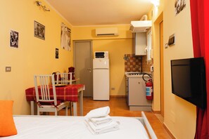 Una habitación de hotel compacta con cama, una mesa de comedor con sillas, kitchenette y televisor.