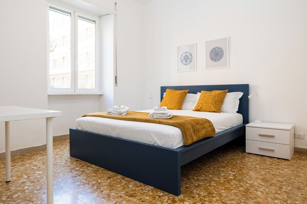 A bedroom with a bed, a bedside table, a nightstand, and a window. - Pandolfo Apartment (Rome)