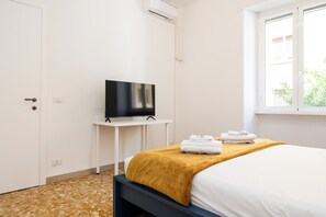 A hotel room with a bed, a TV on a small table, and a window with a view of buildings. - Pandolfo Apartment (Rome)