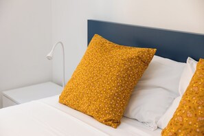 A neatly made bed with white bedding and a mustard-colored pillow with a floral pattern. - Pandolfo Apartment (Rome)