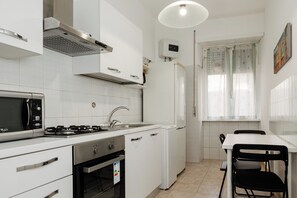 A compact kitchen with white cabinets, a microwave, stove, oven, and a small dining area with a table and chairs. - Pandolfo Apartment (Rome)