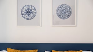 Ein Schlafzimmer mit zwei gerahmten Wandbildern in blau und weiß, einem blauen Kopfteil und zwei Kissen mit einem gelben Blumenmuster.