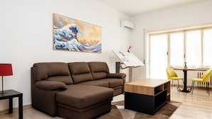 A living room with a brown sectional sofa, a wooden coffee table, a red floor lamp, and a painting of a wave on the wall. - Vatican Giulianos House (Rome)