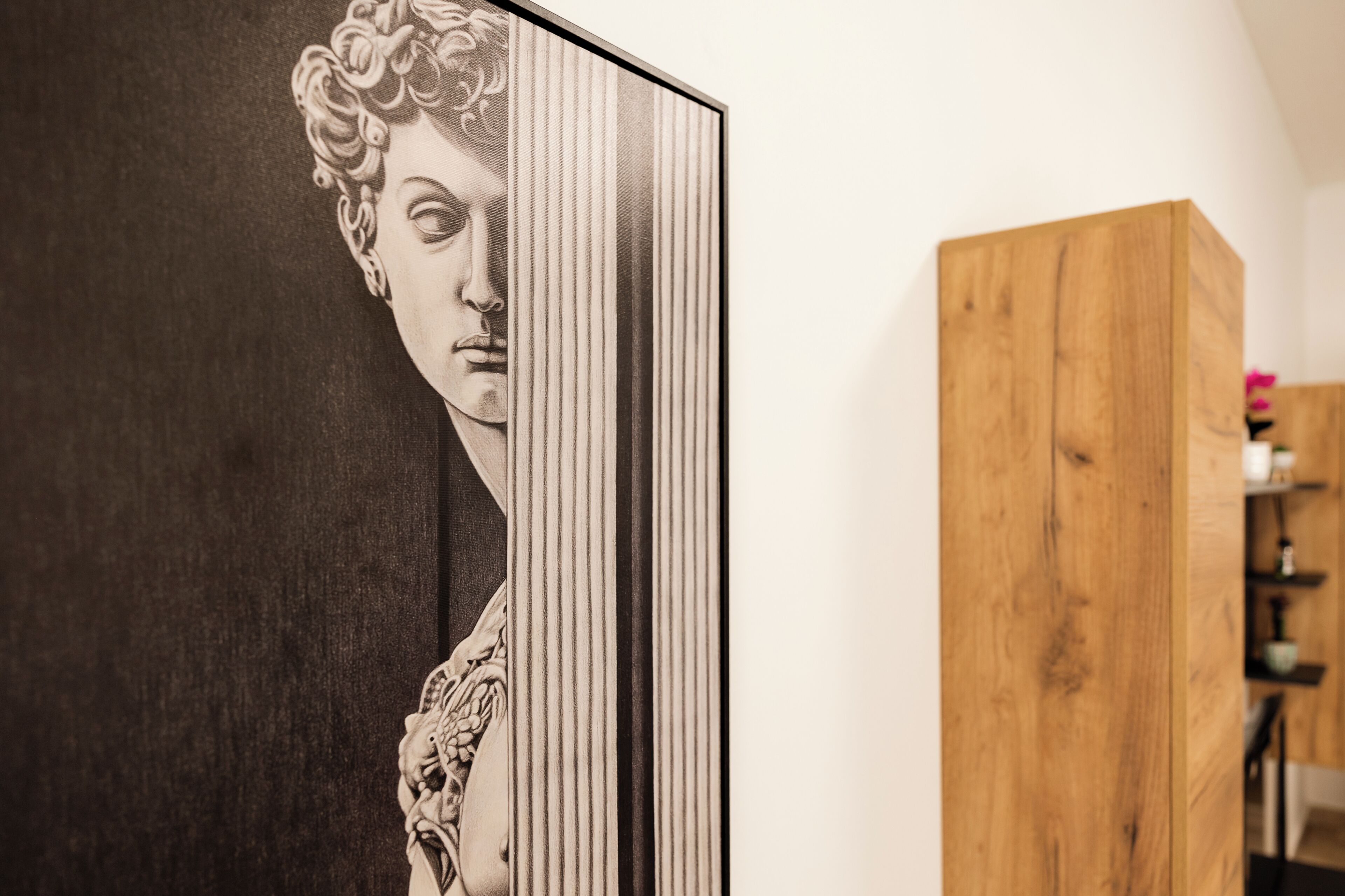 Een lijst met een kunstwerk waarop een klassiek figuur afgebeeld is, een houten kast en een witte muur.