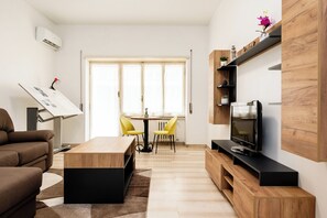 A modern living room with a sofa, a coffee table, a TV on a wooden stand, and a dining area with a table and chairs. - Vatican Giulianos House (Rome)