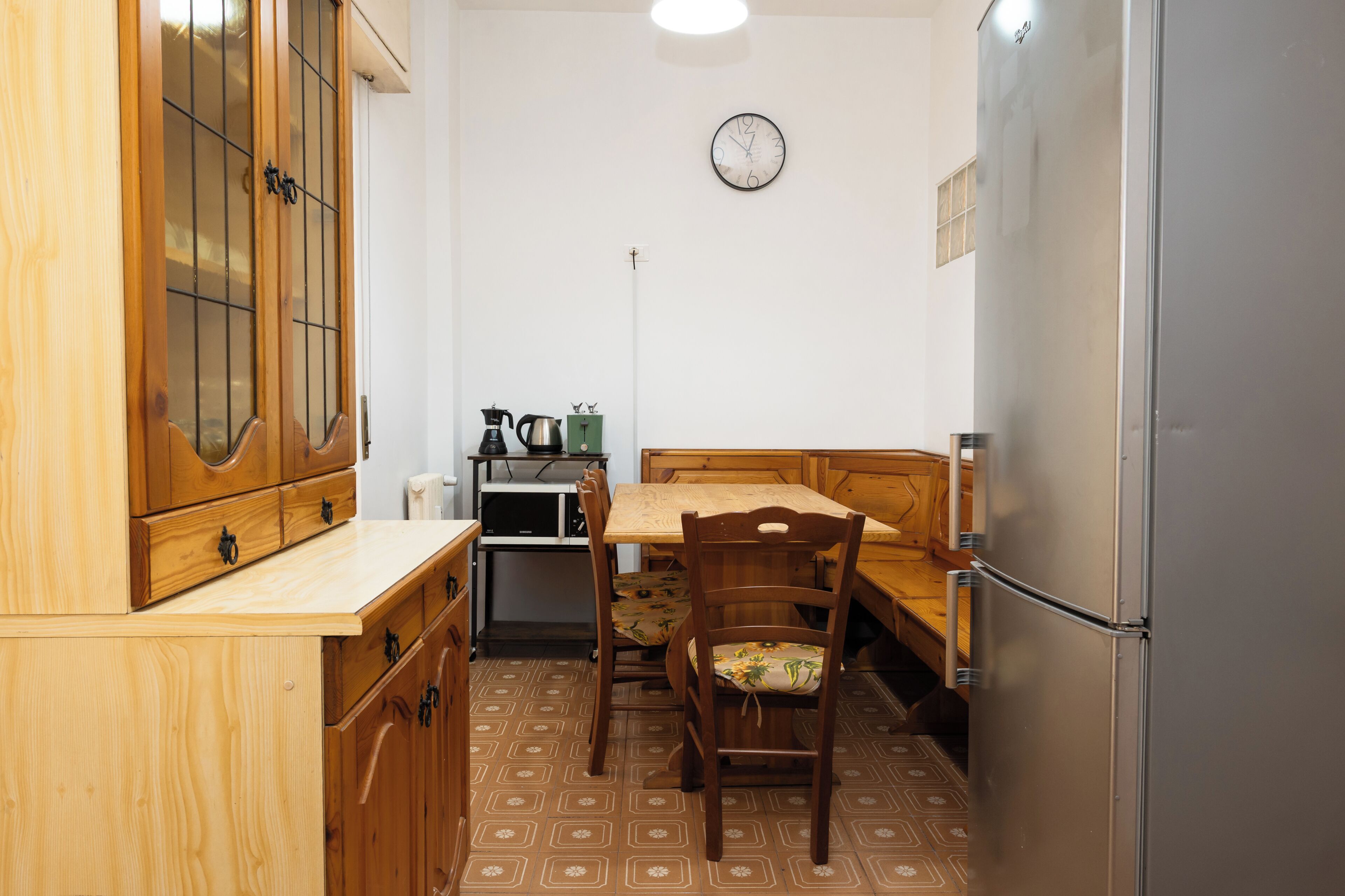 A compact kitchen with wooden cabinets, a dining table, and a refrigerator.