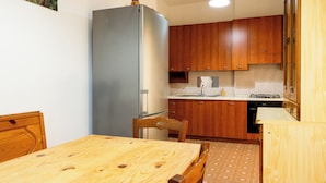 A compact kitchen with wooden cabinets, a built-in refrigerator, a dining table with chairs, and a patterned floor. - Vatican Giulianos House (Rome)
