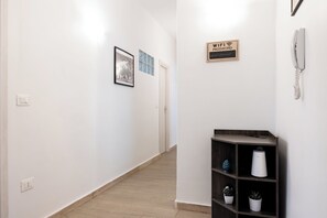 A hallway with a white wall, a framed picture, a WiFi password sign, a phone, and a shelf with plants. - Vatican Giulianos House (Rome)