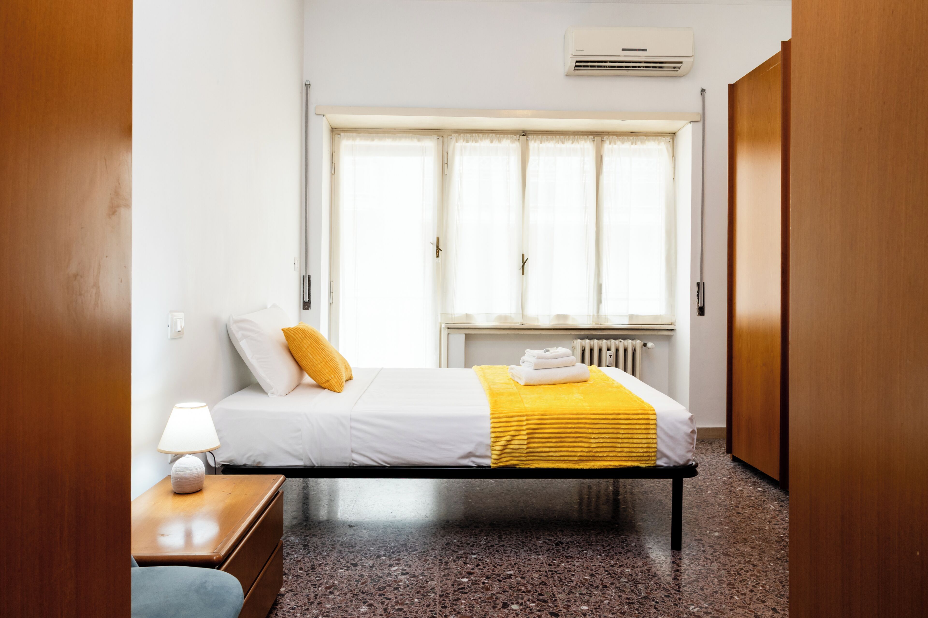 Une chambre d’hôtel avec un lit, une table de chevet, une fenêtre avec des rideaux et un radiateur.