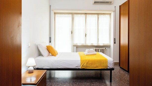 A hotel room with a bed, a nightstand, a window with curtains, and a radiator. - Vatican Giulianos House (Rome)