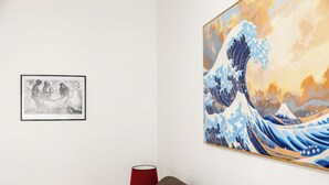 A room with a large painting of a wave, a framed black and white photo, and a red lamp on a side table. - Vatican Giulianos House (Rome)