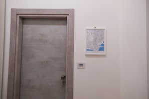Eine geschlossene Tür mit einfachem Griff, ein an der Wand montierter Lichtschalter und eine gerahmte Karte an der Wand.