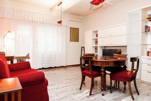 Ein Zimmer mit einem Esstisch, Stühlen, einem roten Sofa, einer Lampe und einem Bücherregal.
