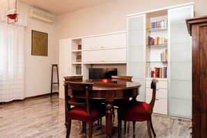A dining area with a wooden table and chairs, a television, and a bookshelf with books. - La Terrazza di Maria Pia (Rome)
