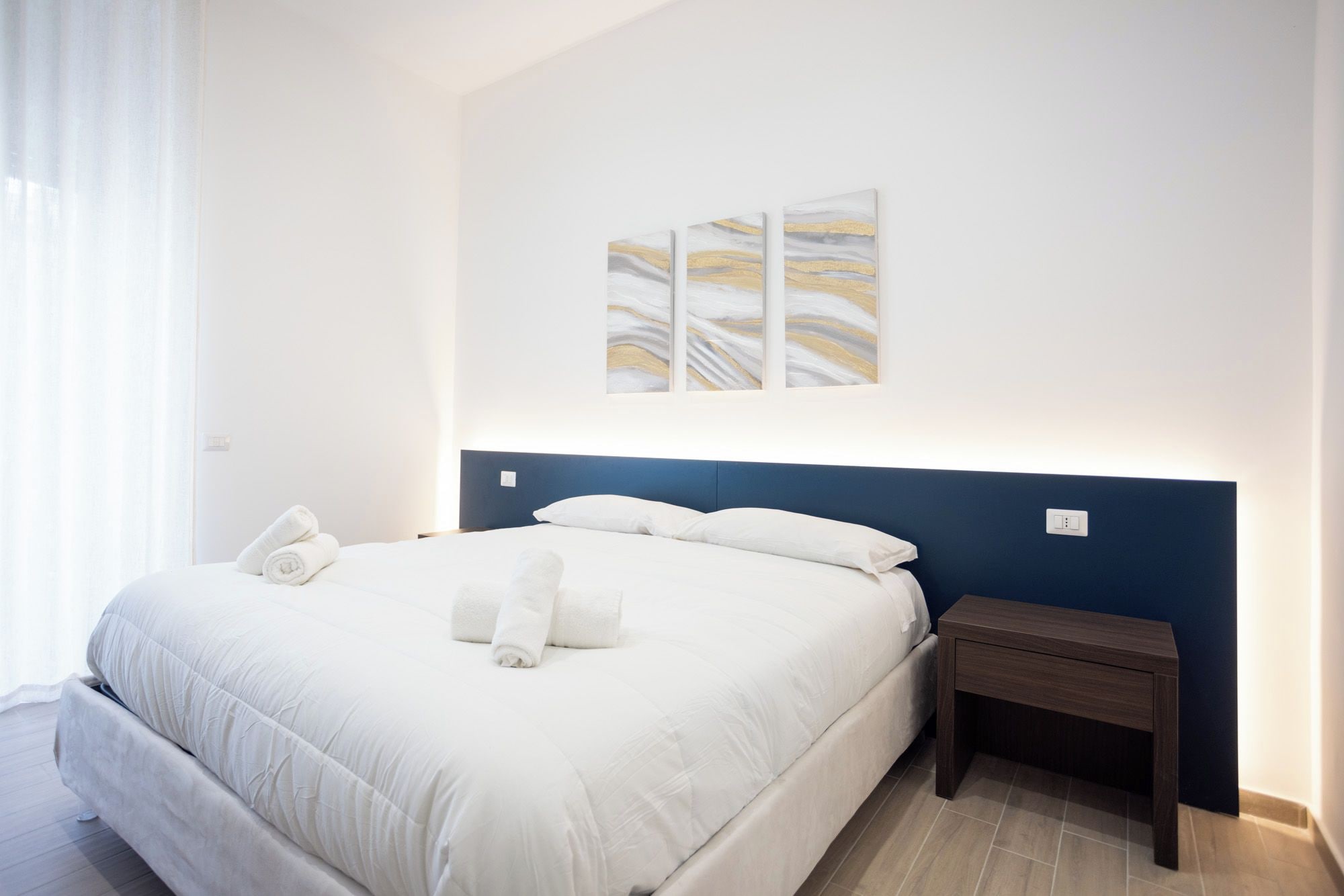 Una habitación de hotel con una cama grande, una mesita de noche y una obra de arte colgada en la pared.