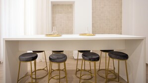 A white dining table with four black bar stools, a glass vase, and a gold tray. - Palazzo Pepe (Naples)