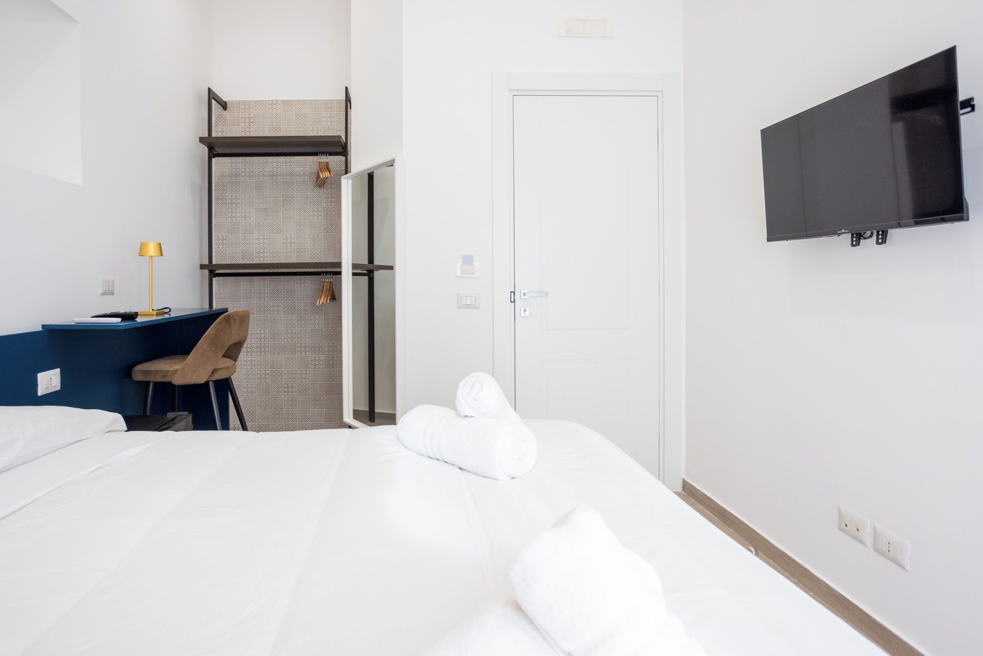 Habitación de hotel con cama, escritorio con silla, televisor montado en la pared y una puerta.