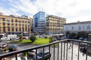A city street with parked cars, a pedestrian, and buildings including a modern high-rise and older residential structures. - Palazzo Pepe (Naples)