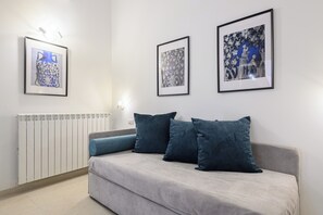 Un salon moderne avec un canapé gris, deux coussins bleu foncé et trois œuvres d’art encadrées accrochées au mur.