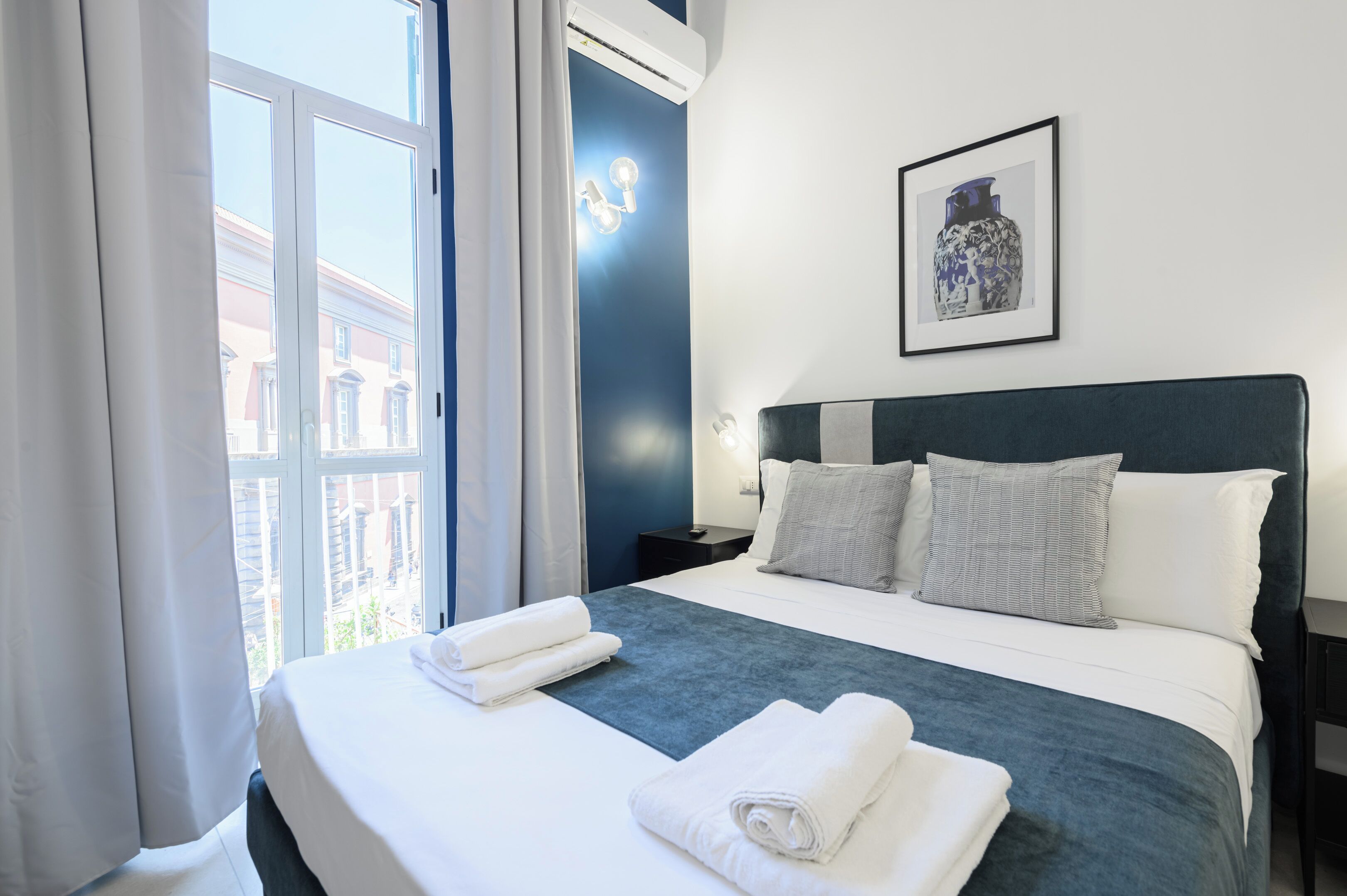 A hotel room with a large bed, white linens, a dark headboard, and a framed picture on the wall.