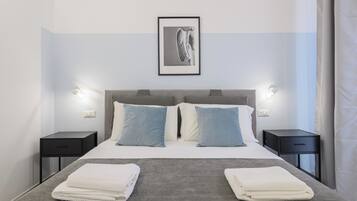 A modern hotel room with a neatly made bed, two bedside tables, and a framed artwork above the bed.