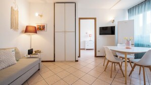 Una sala moderna con sofá, una mesa de comedor con sillas, televisor y armario.
