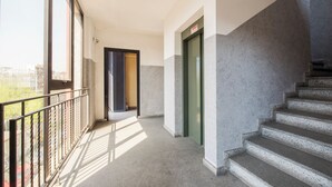 Un pasillo con una escalera, un balcón con barandilla de metal y una puerta con un cartel.