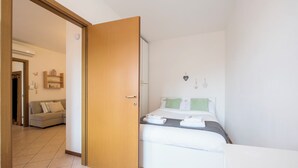 Una habitación de hotel con cama, mesita de noche, armario y un sofá en la zona de estar contigua.