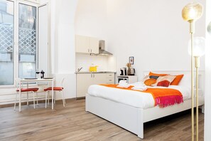 Een moderne slaapkamer met een wit bed, een oranje plaid en een zithoek met een gele stoel.