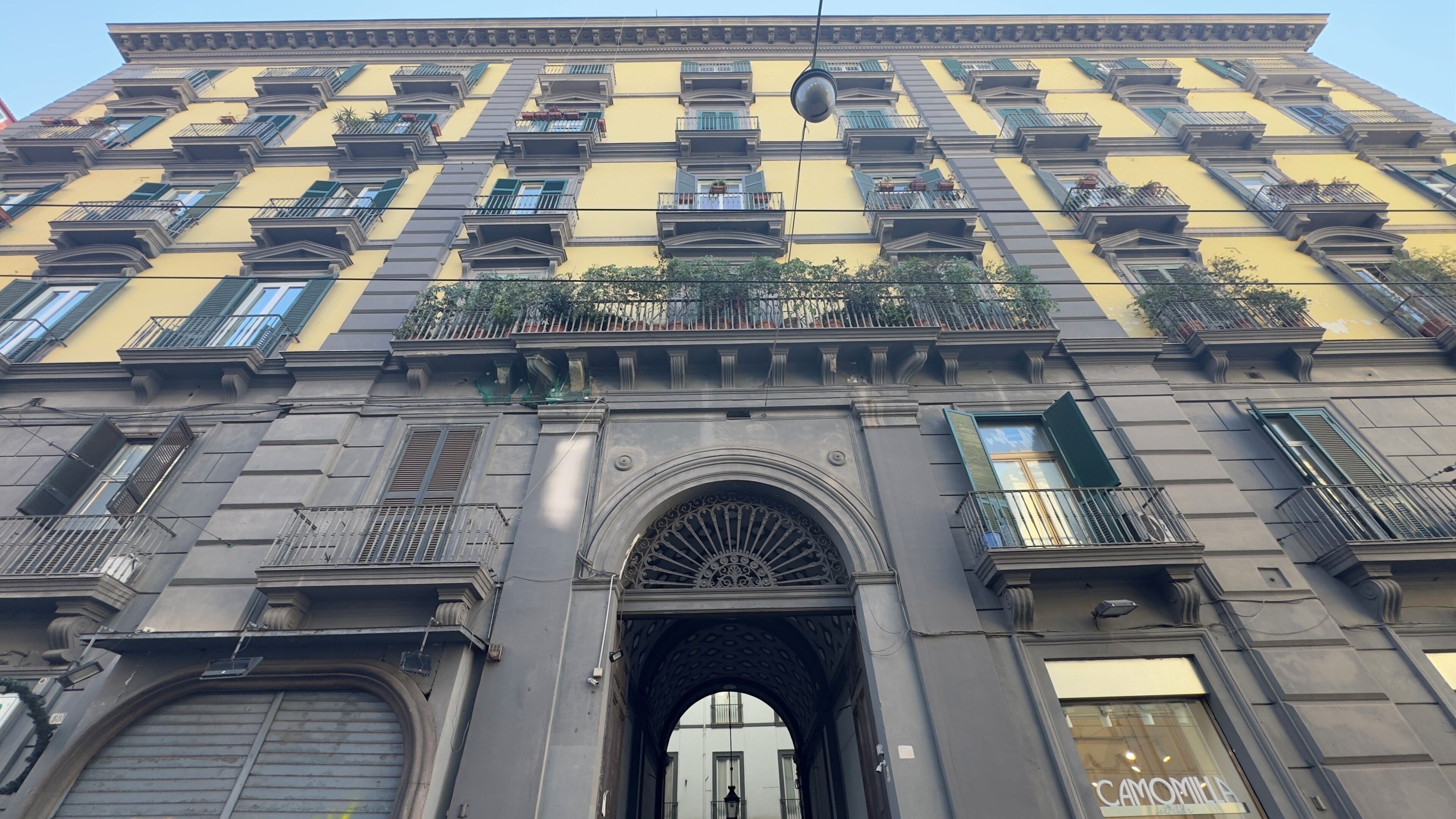 A multi-story building with a central archway entrance, balconies with railings, and a yellow facade.