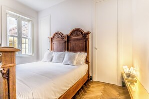 A bedroom with a wooden bed, white bedding, a wooden nightstand, a window with a view, and a door. - EVA Loft (Rome)