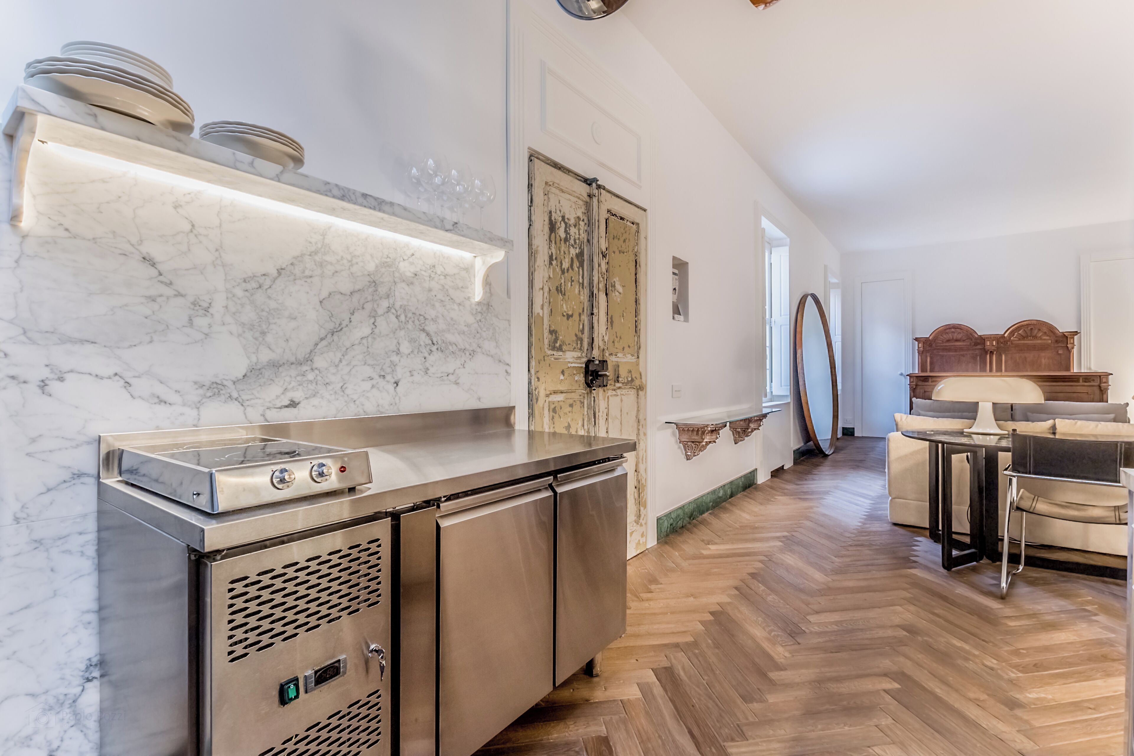 Una cocina moderna con encimera de mármol, electrodomésticos de acero inoxidable y suelo de madera con patrón de espiga.