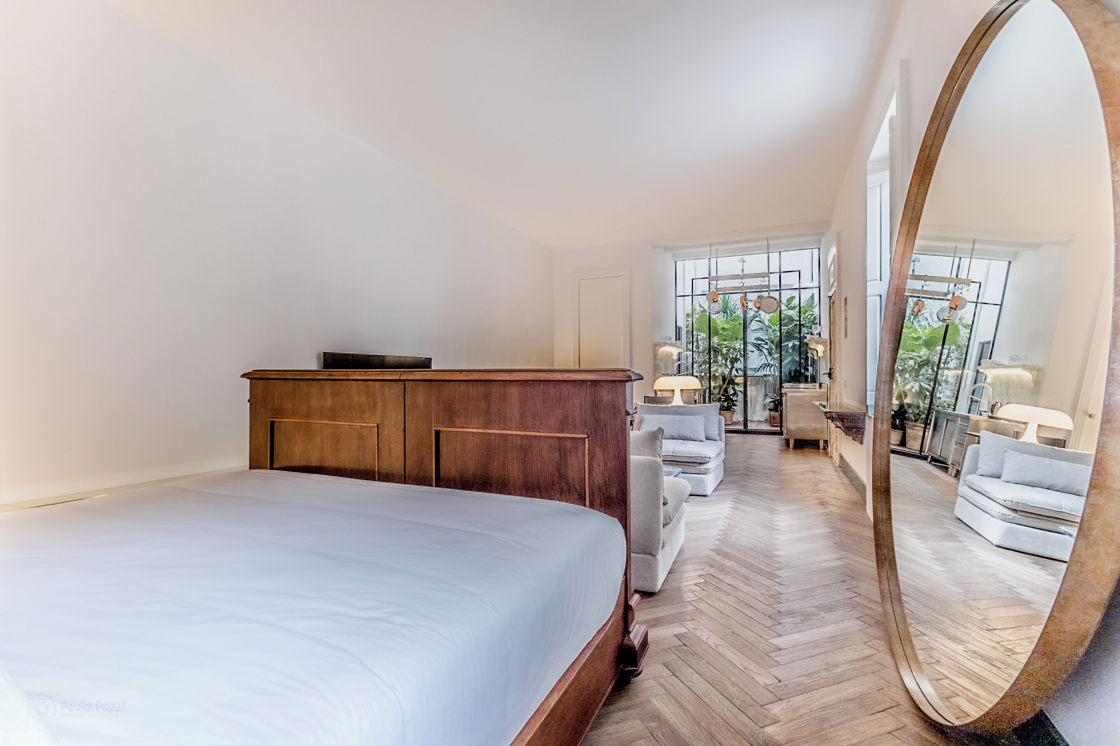 Un dormitorio con una cama grande, cómoda de madera y un espejo. Cuenta con una zona de estar con sofá y sillones.