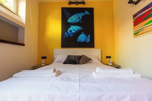 Ein Hotelzimmer mit einem Bett, zwei Nachttischen, einem an der Wand befestigten Kunstwerk mit Fischen und einem farbenfrohen abstrakten Gemälde.