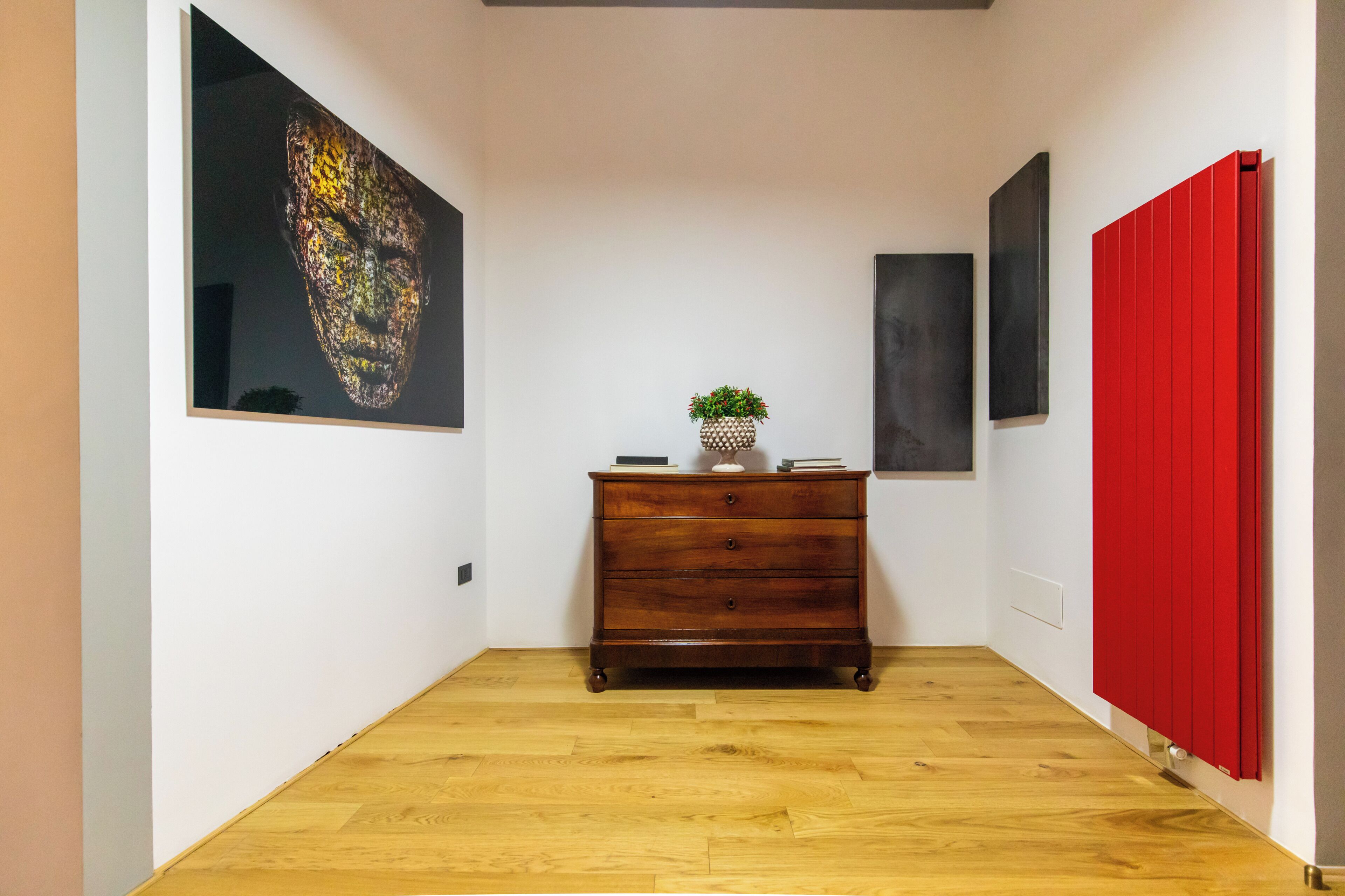 Un pasillo con piso de madera, un aparador de madera oscura con una planta y un radiador rojo.