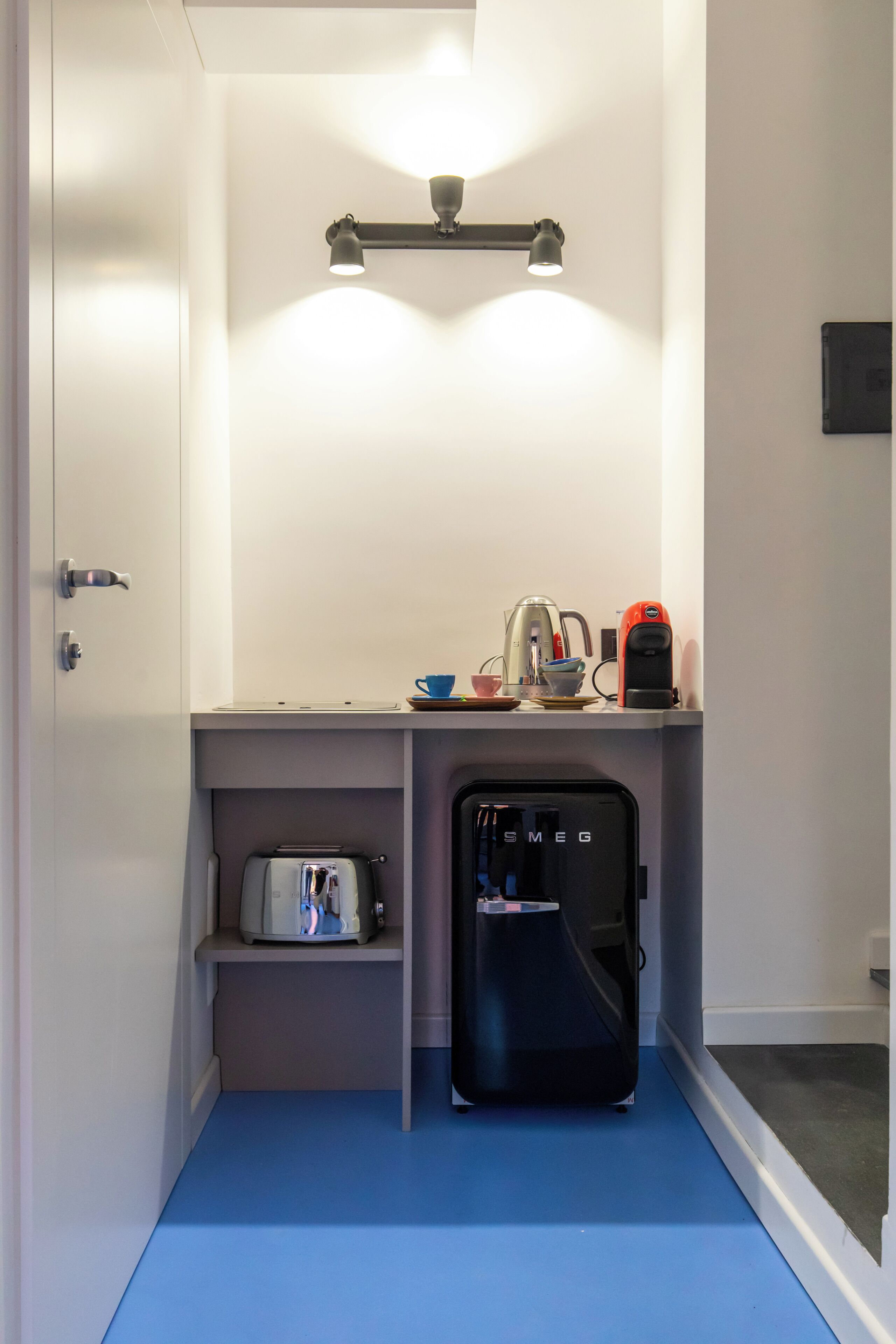Una kitchenette compacta con refrigerador, cafetera y hervidor.