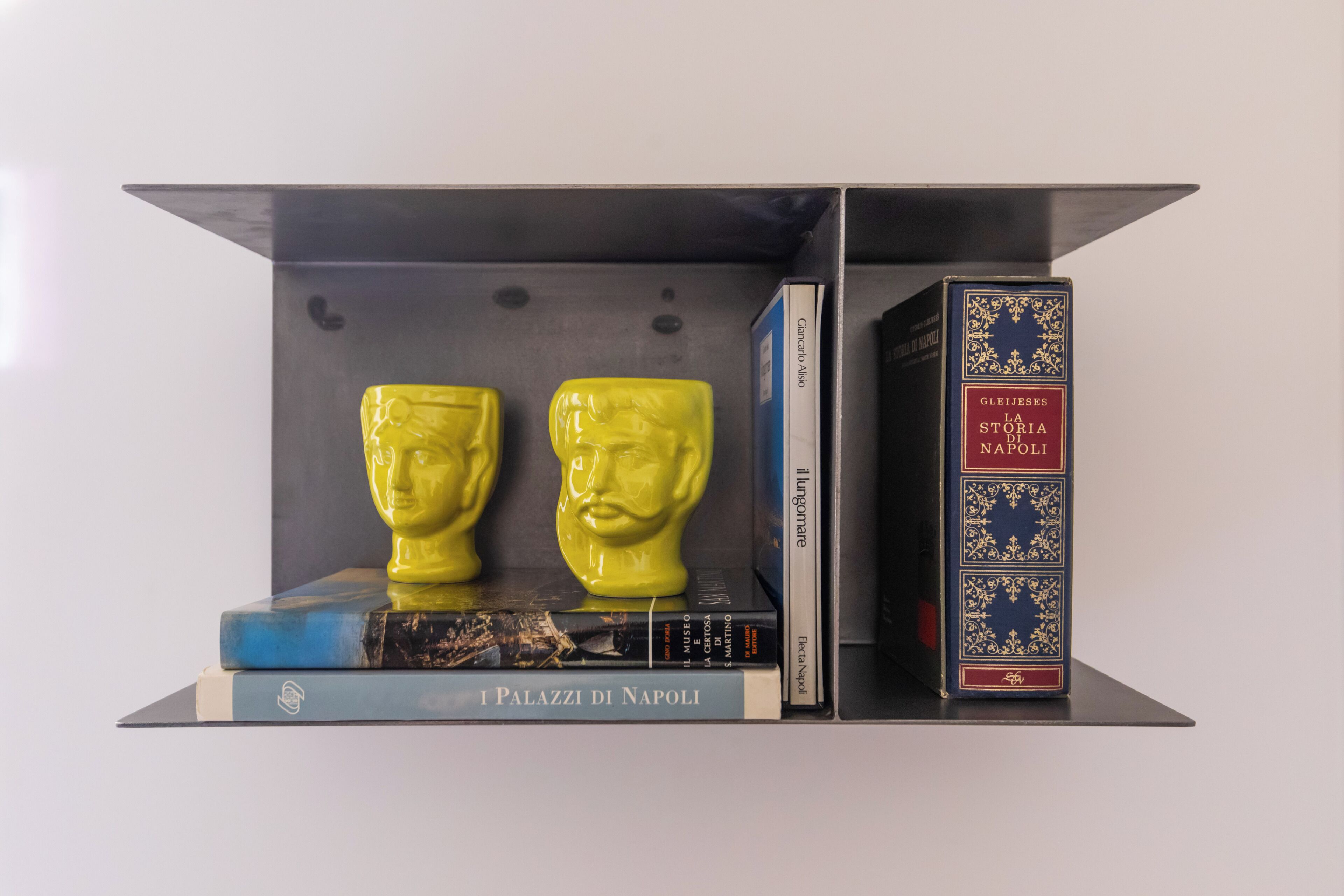 A bookshelf with books and two yellow bust sculptures.