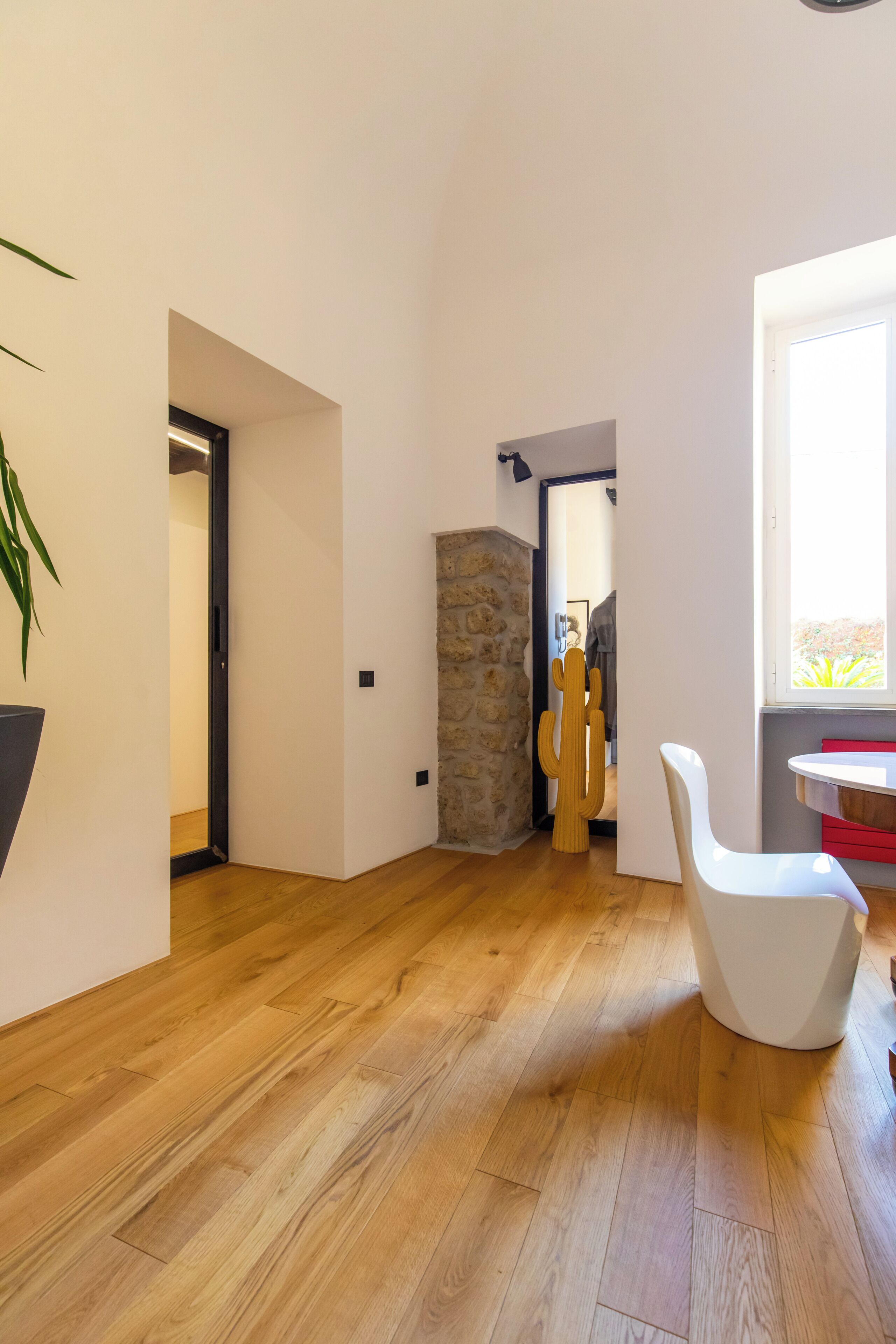 A modern interior with a wooden floor, a cactus sculpture, and a white chair.