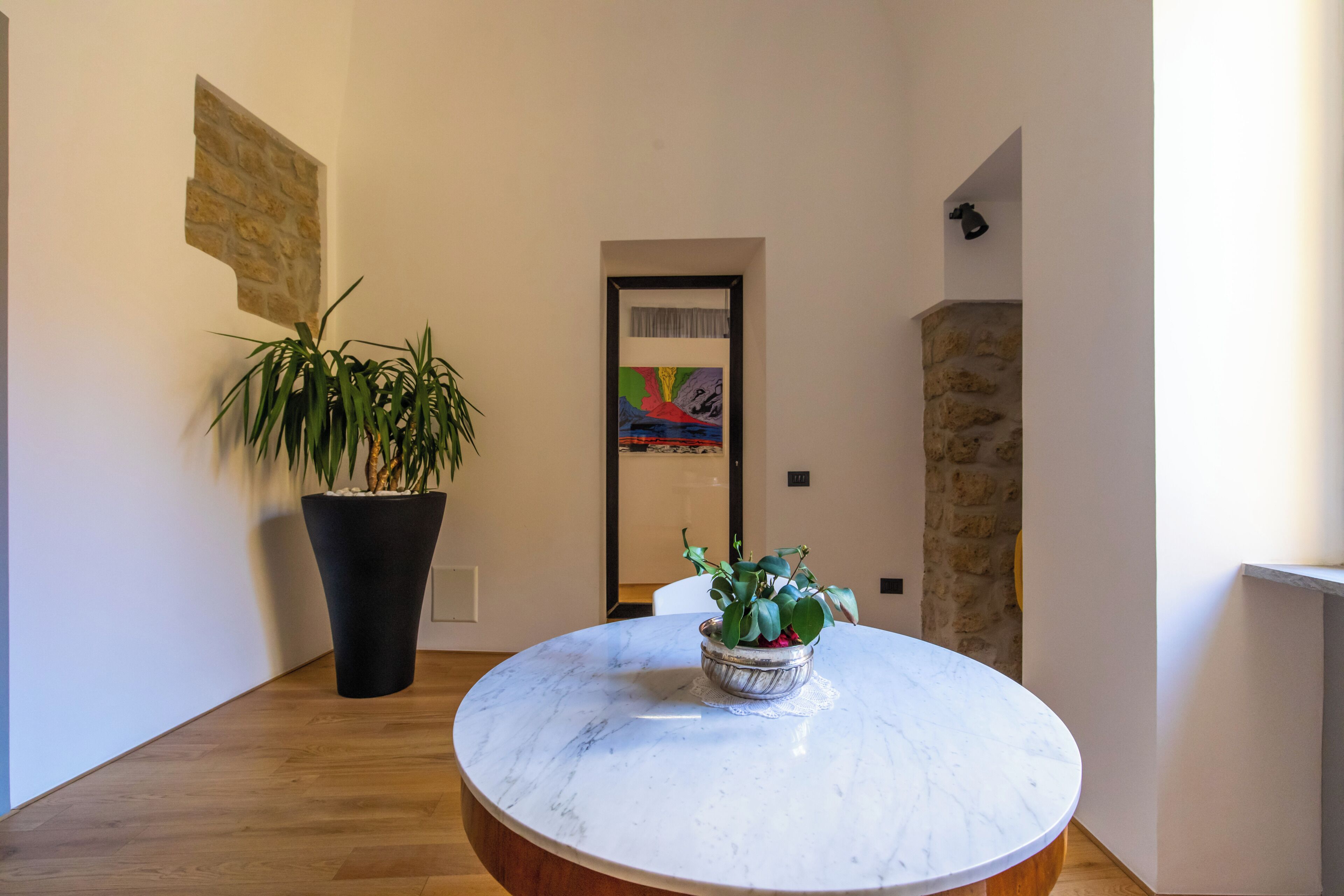 Un interno moderno con un tavolo rotondo in marmo, una grande pianta in vaso e un quadro colorato appeso alla parete.