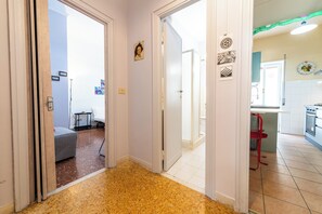 Ein Flur, der zu einem Schlafzimmer mit Bett und kleinem Tisch, einer Küche mit rotem Stuhl und einem Essbereich mit Tisch und Stühlen führt.