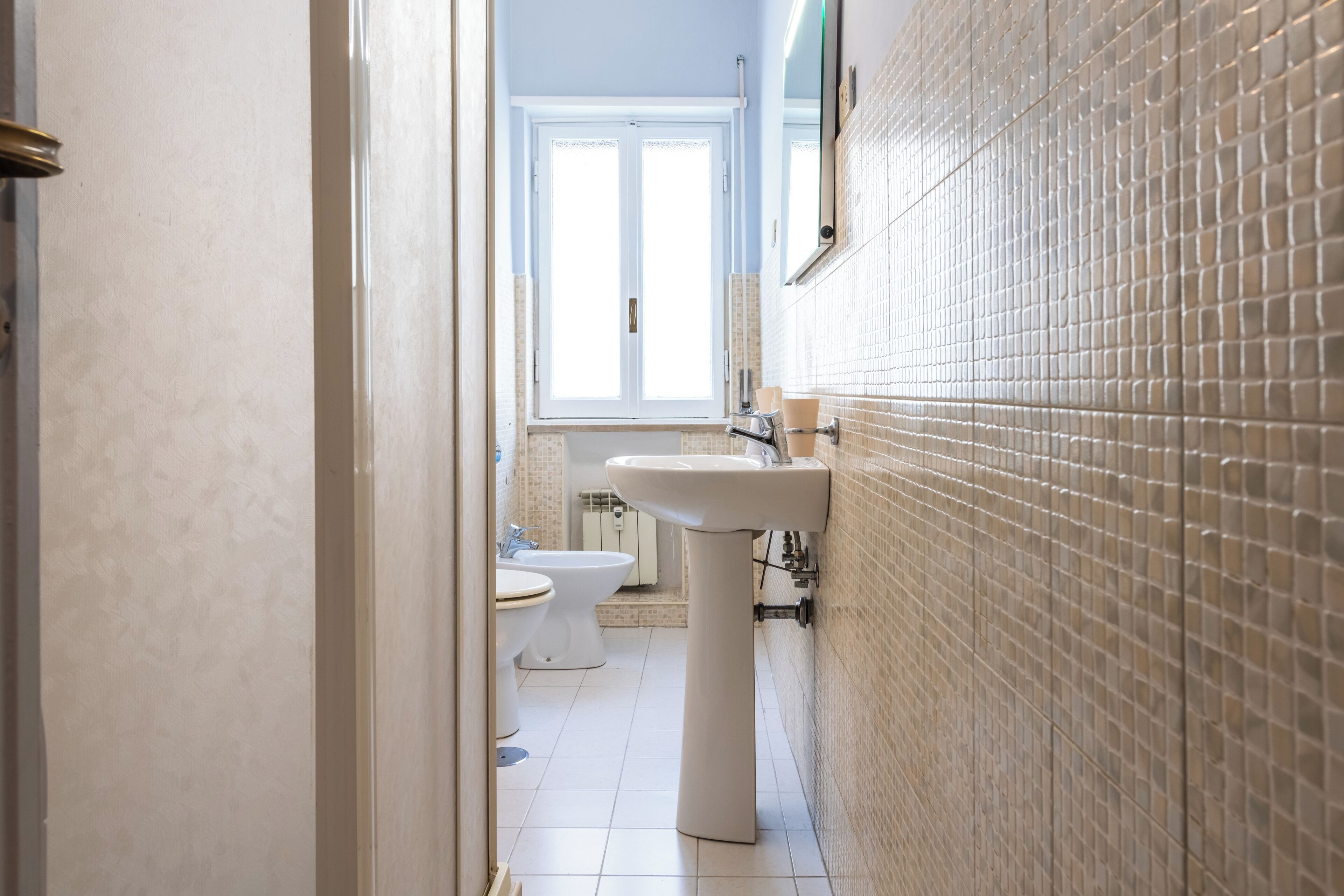 A bathroom with a white sink, two toilets, and a window.