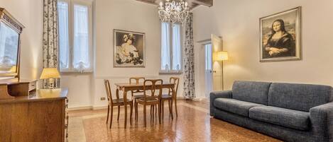 A spacious living room with a wooden dining table, blue sofa, and a chandelier.