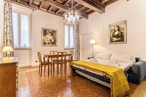 A room with a bed, a chandelier, a dining table with chairs, and two paintings on the walls. - Casa Iside (Rome)