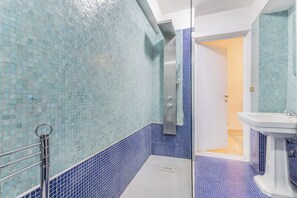 A bathroom with blue mosaic tiles, a shower area, and a white sink. - Casa Iside (Rome)