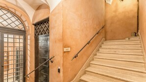 A staircase with a handrail, a door with a metal grille, and a wall with a textured finish. - Casa Iside (Rome)