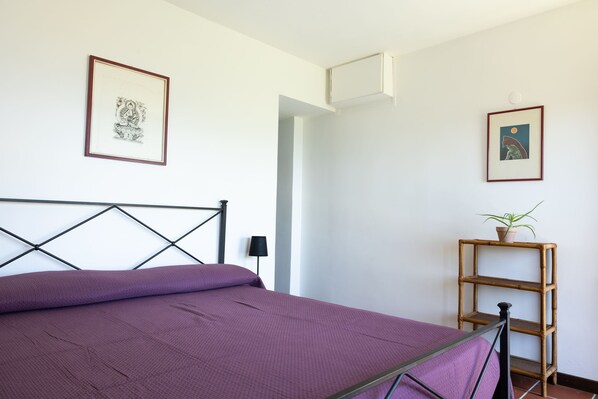 Un dormitorio con cama, repisa con planta y cuadros en las paredes.