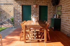 Una mesa de madera con sillas, un jarrón con flores y una puerta verde en un edificio de ladrillo.