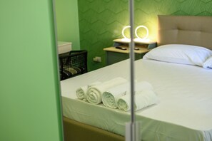 Ein Hotelzimmer mit einem ordentlich bezogenen Bett, einem Nachttisch mit Lampe und einer Wand mit grünem Muster.